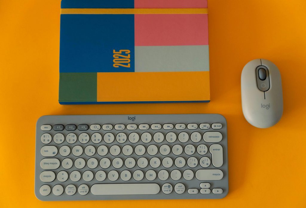 Flat lay of a 2025 planner, keyboard, and mouse on a vibrant yellow background.